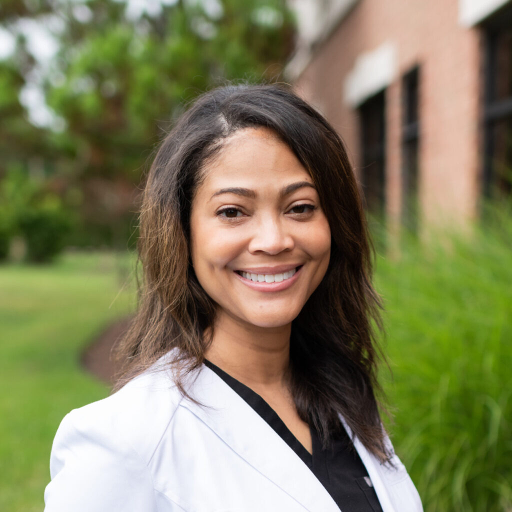 Portrait of Orthodontist: Dr. Woodard in her white coat on a lawn by the side of a brick building