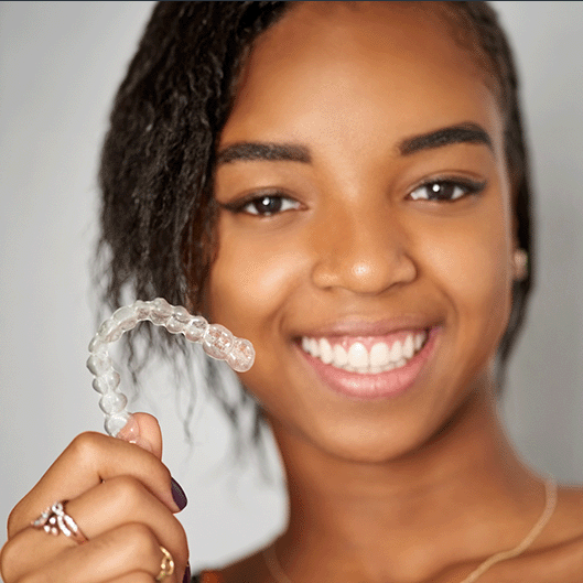 Teen with Invisalign Teen® in Suffolk, VA holding her clear aligner in her right hand and smiling