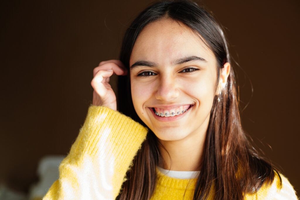 Teen with braces in Chesapeake, VA smiling while tucking her brown hair behind her ear