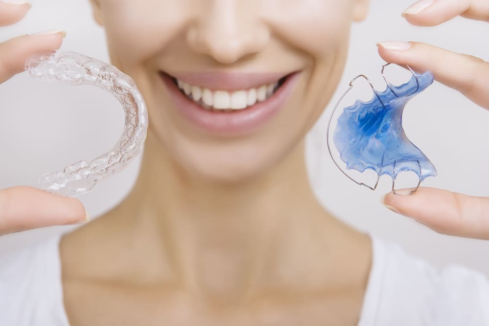 Woman holding 2 orthodontic retainers in Chesapeake, VA, one hawley retainer and one clear retainer